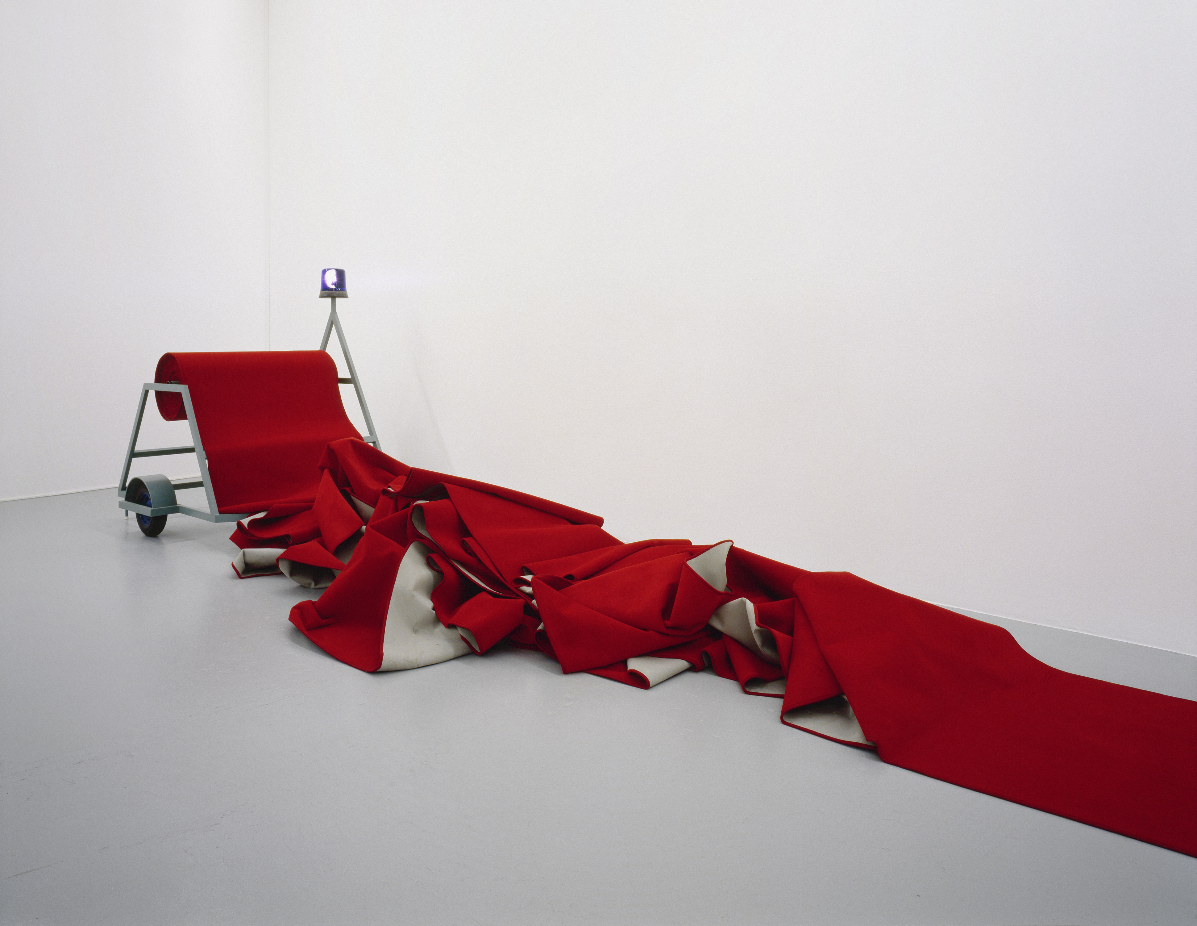 Fabrice Gygi, Dérouleur de tapis rouge, 1999
Stahl lackiert, Blaulicht, Teppich, Gummiräder, Grösse variabel
Sammlung Migros Museum für Gegenwartskunst